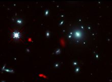 The galaxy cluster RXCJ0600-2007 taken by the NASA/ESA Hubble Space Telescope, combined with gravitational lensing images of the distant galaxy RXCJ0600-z6, 12.4 billion light-years away, observed by ALMA (shown in red). Due to the gravitational lensing effect by the galaxy cluster, the image of RXCJ0600-z6 was intensified and magnified, and appeared to be divided into three or more parts. Credit: ALMA (ESO/NAOJ/NRAO), Fujimoto et al., NASA/ESA Hubble Space Telescope